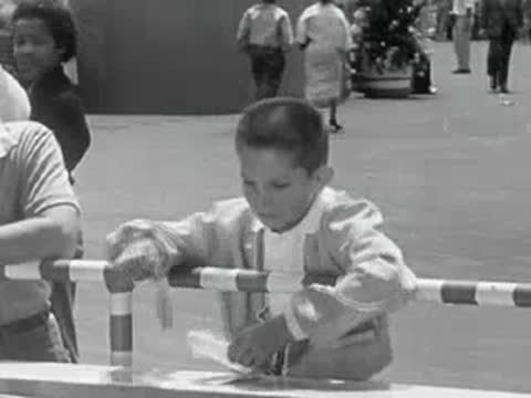 A young boy leaning on a railing at an amusement park attraction.