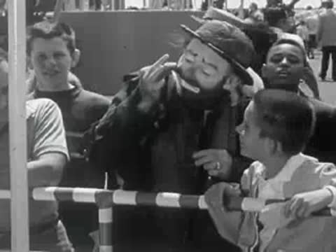 A clown talking with a young boy by the animal enclosure railing.