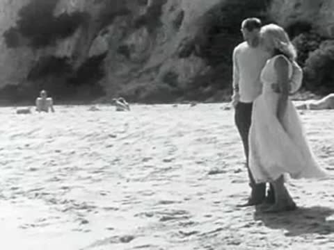 A couple stands together on a sandy beach near the water.
