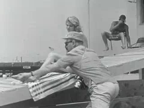 A photographer in uniform takes pictures of a woman posing in a swimsuit by the coast.