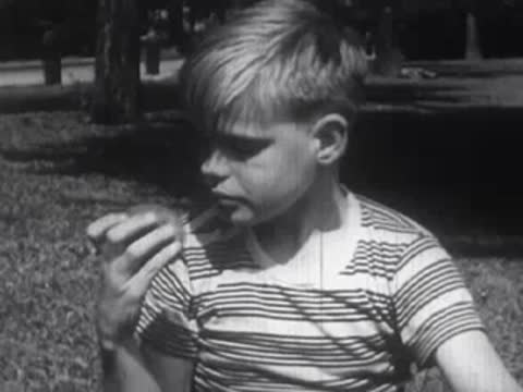 Young boy wearing a striped t-shirt outdoors, looking sideways and eating.