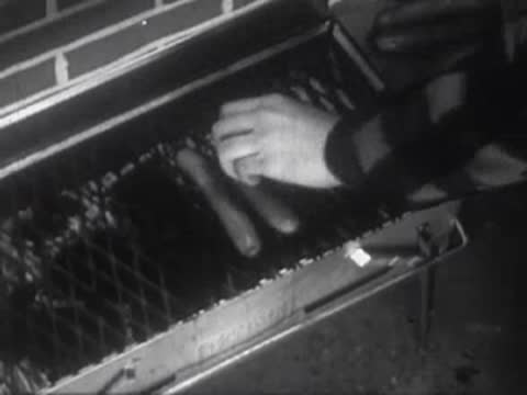 Hands grilling sausages on an outdoor barbecue grill.
