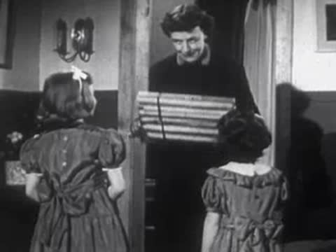 Children presenting a wrapped gift box to a woman indoors.