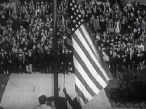 Two people raising an American flag on a flagpole outside.
