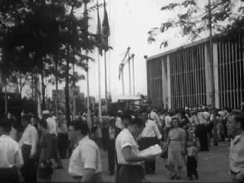 Crowd of people walking outside near buildings and flags.