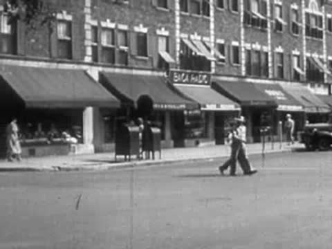 People walking along a city sidewalk past storefronts.