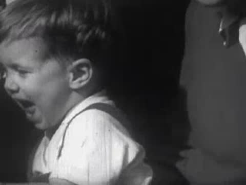 Close-up of a toddler crying with mouth open wide indoors or in shadow.