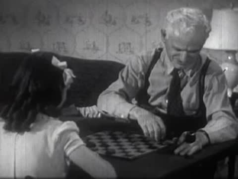 Older man and a young girl playing a game of checkers indoors at table.