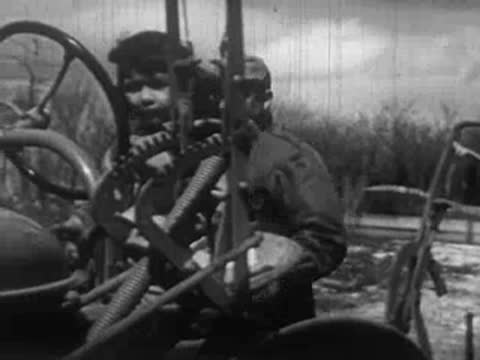 Man walking on a dirt path, followed by a man and child on tractor.