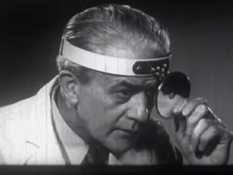 Man wearing a medical head mirror examining something in an office.