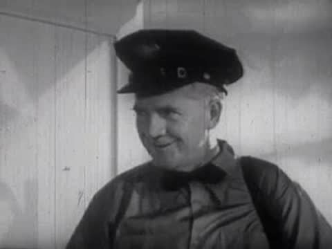 Man wearing a uniform cap and bow tie smiling slightly indoors.