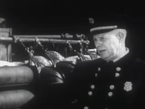 A man in uniform wearing a cap stands outdoors near equipment, looking upwards.