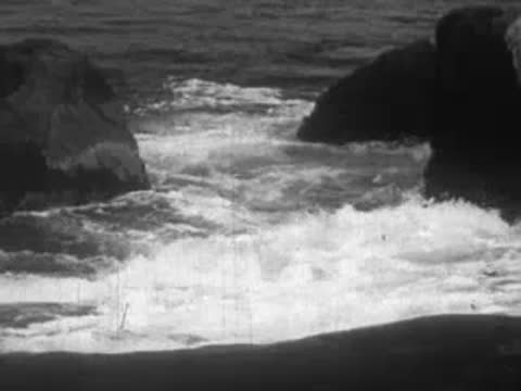 Ocean waves powerfully crashing against large dark rocks near the shore.