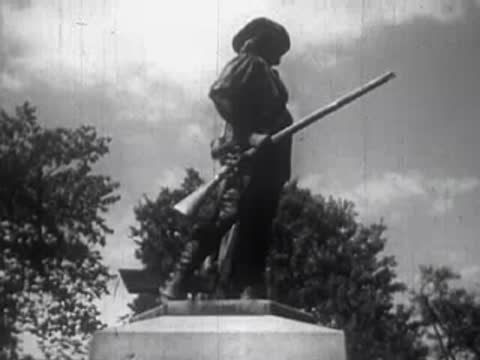A statue of a historical figure holding a rifle outdoors against the sky.