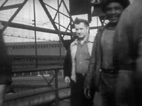 Men walking across an industrial bridge structure outdoors during the day.