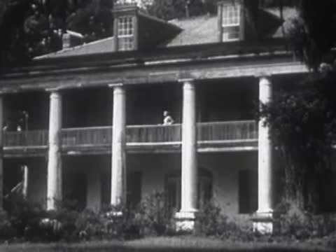 A large two-story plantation house with white columns and a second-floor balcony.