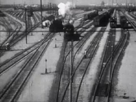 A busy railroad yard with steam locomotives and parallel train tracks.