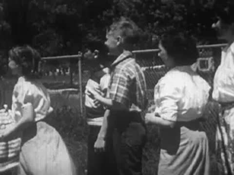 Group of children and a woman gathered outdoors near a chain-link fence.