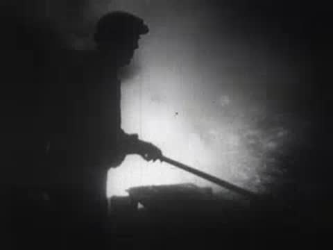 Industrial workers in a foundry stirring molten metal with sparks flying.