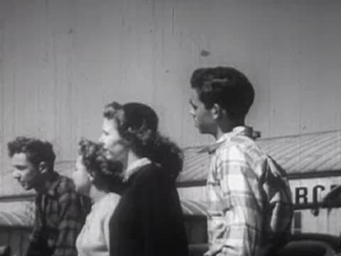 Four teenagers, three boys and one girl, standing outside together chatting.