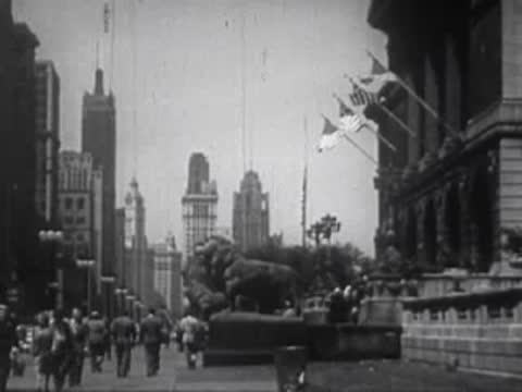 Busy city street lined with tall buildings, lion statues, and American flags