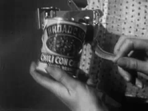 Hands opening a can of chili con beans using a wall-mounted can opener