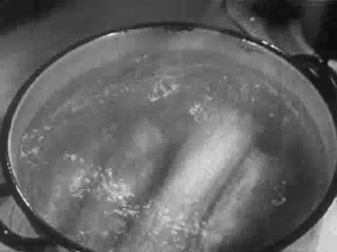 Pot of boiling water on a stove with corn cobs being added