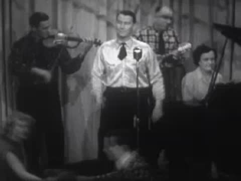 Band performing on a stage with singers, musicians, and a piano.