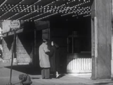 Couple standing outside a building entrance beneath a marquee light display.