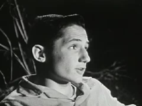 Close-up of a young man speaking animatedly near a campfire