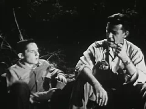 Two young men talking together near a campfire at night