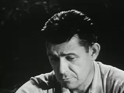 Close-up of a man speaking and looking down near a campfire
