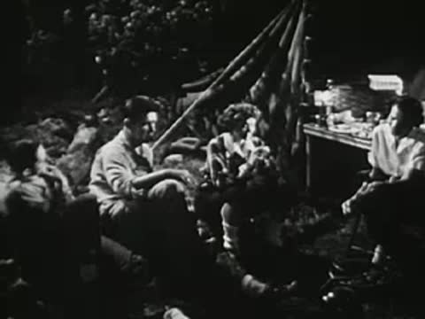 Medium shot of young people socializing around a campsite at night