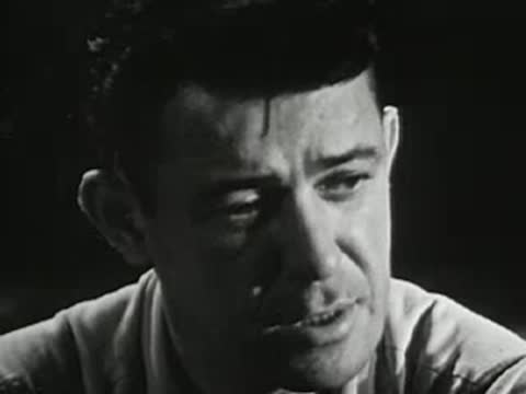 Man speaking near a campfire at night, mid-20th-century apparel
