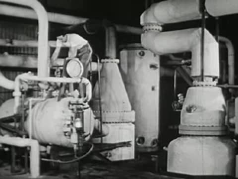 Industrial plant interior with large tanks, pipes, and worker checking machinery