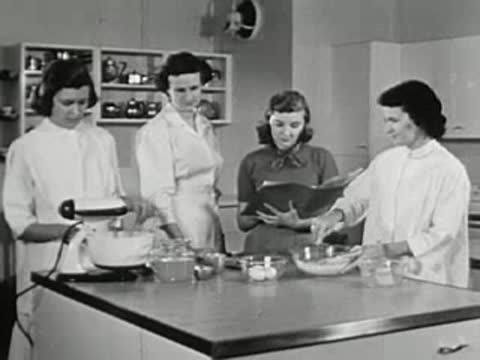 Group of women in white coats using an electric mixer in a kitchen laboratory