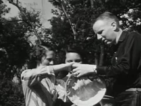 People examining a cloth bag outdoors in a park or wooded area, vintage attire