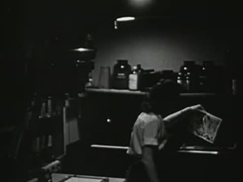 Person working in a dark room with photographic equipment, developing film or prints