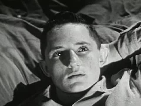 A young man lying on his back, looking up pensively in a dimly lit scene.