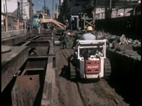 A small tracked loader moving earth and debris in a deep trench.