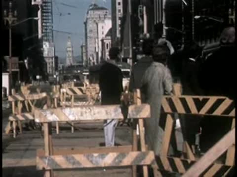 Construction workers and equipment near wooden barriers on a city street.