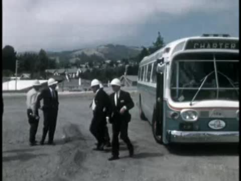 People boarding a vintage charter bus parked on a gravel lot.