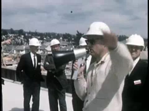 A construction foreman speaking into a megaphone while wearing a hard hat.