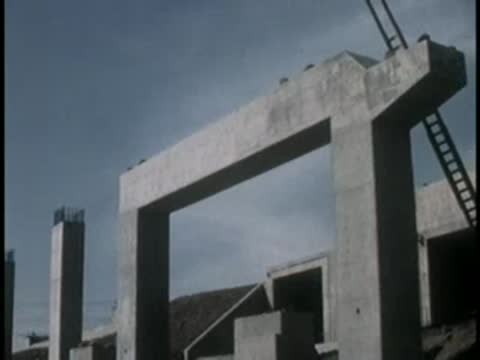 Large precast concrete bridge bents and pillars under a cloudy sky.