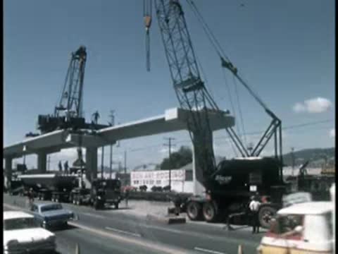 Cranes lifting and positioning large concrete bridge segments over a highway.