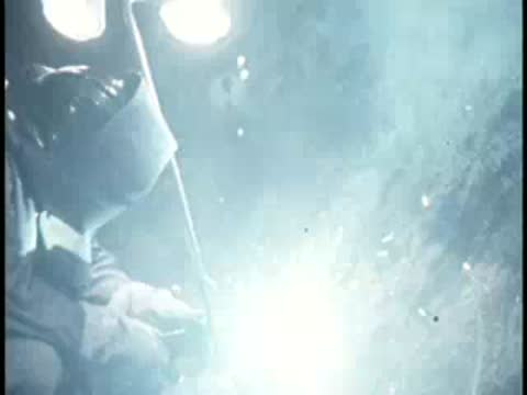 A worker wearing a protective welding mask welding metal components with sparks.