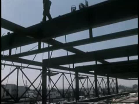 A construction worker walking along an elevated steel beam framework.