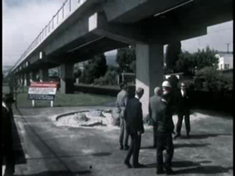 Men in suits and hard hats walking around a landscaped highway pillar base.