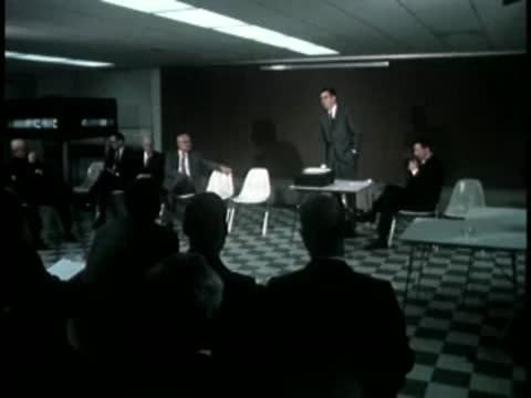 A speaker presenting to an audience seated in a modern meeting room.