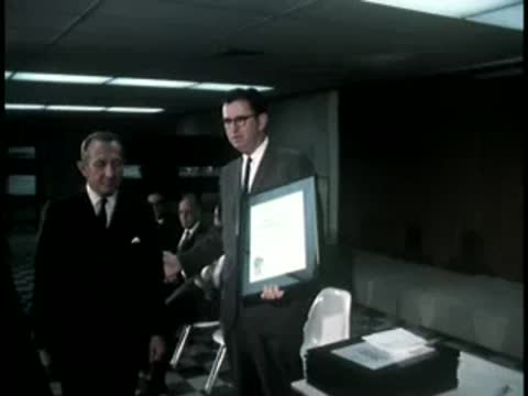 Men in suits holding a framed certificate indoors